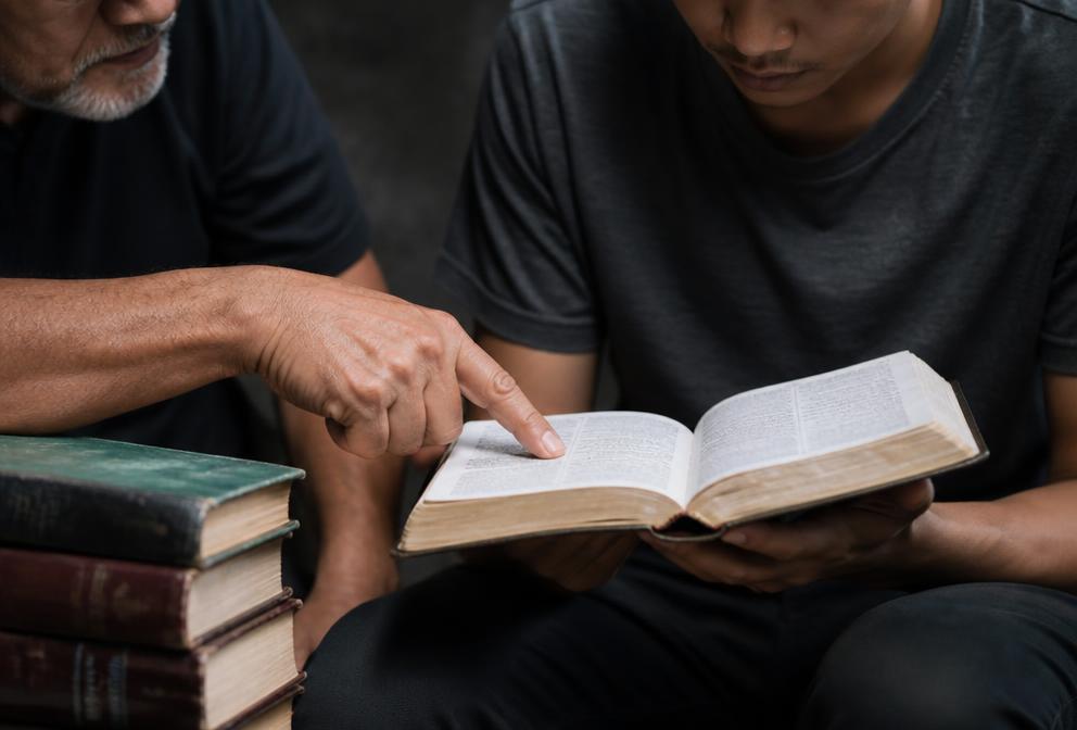 Un hombre mayor enseñando la Biblia a un joven estudiante